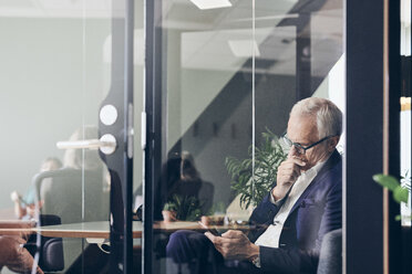 Älterer männlicher Manager, der ein Smartphone benutzt, gesehen durch eine Glaswand im Kreativbüro - MASF12345