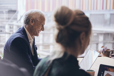 Smiling mature businessman using laptop by businesswoman at creative office - MASF12354