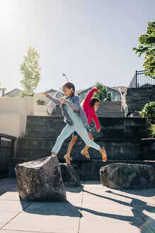 Mixed Race sisters jumping on rocks - BLEF01228