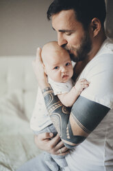 Kaukasischer Vater mit Tätowierungen auf den Armen, der seinen kleinen Sohn küsst - BLEF01257