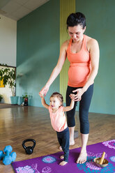 Mixed Race expectant mother holding hands of daughter on exercise mat - BLEF01284