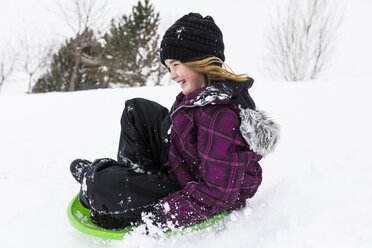Lächelndes Mädchen rutscht auf einem Schlitten im Schnee - BLEF01301