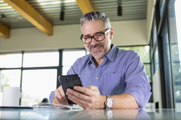 Kaukasischer Mann, der am Tisch eine SMS auf seinem Handy schreibt - BLEF01309