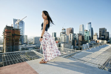 Lächelnde asiatische Frau auf einem windigen städtischen Dach stehend - BLEF01332