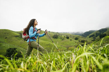 Smiling mixed race woman hiking with walking sticks - BLEF01399