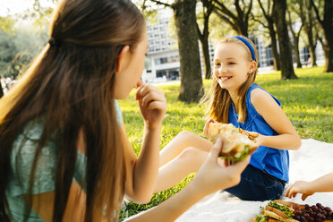 Smiling Caucasian sisters eating food at picnic - BLEF01403