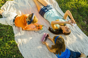 Caucasian brother and sisters laying on blanket in park using technology - BLEF01417