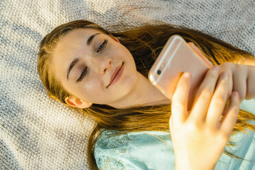 Kaukasisches Mädchen liegt auf einer Decke und schreibt eine SMS auf einem Handy - BLEF01418