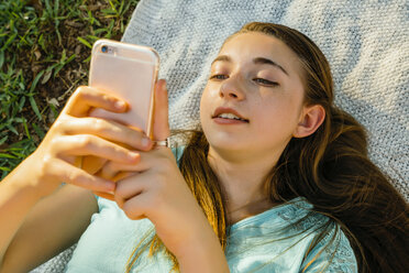 Kaukasisches Mädchen liegt auf einer Decke und schreibt eine SMS auf einem Handy - BLEF01420