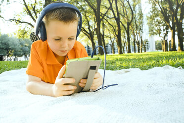 Serious Caucasian boy laying on blanket in park listening to digital tablet - BLEF01425