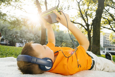 Kaukasischer Junge liegt auf einer Decke im Park und hört einem digitalen Tablet zu - BLEF01428