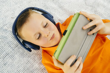 Lächelnder kaukasischer Junge liegt auf einer Decke und hört einem digitalen Tablet zu - BLEF01429