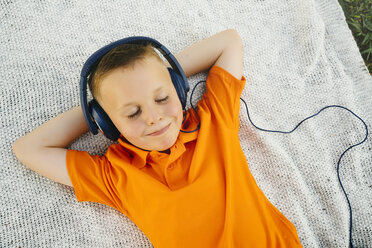 Smiling Caucasian boy laying on blanket in park listening to headphones - BLEF01430