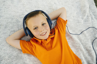 Lächelnder kaukasischer Junge liegt auf einer Decke im Park und hört Kopfhörer - BLEF01431