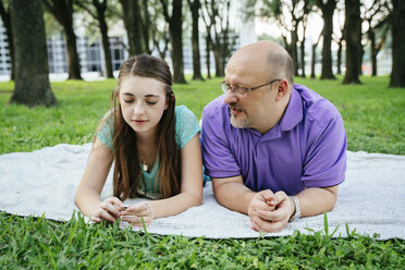 Serious Caucasian father and daughter talking on blanket in park - BLEF01448