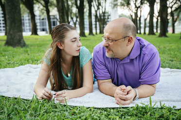 Serious Caucasian father and daughter talking on blanket in park - BLEF01449