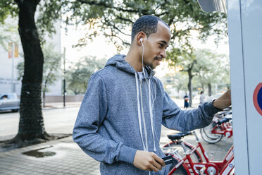 Black man with earbuds paying for bicycle rental with credit card - BLEF01461