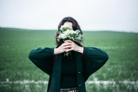 Kaukasische Frau hält Wildblumen vor das Gesicht, lizenzfreies Stockfoto