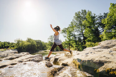 Kaukasische Frau springt auf Felsen in der Nähe des Flusses - BLEF01530