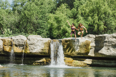 Kaukasisches Paar springt von Felsen in der Nähe von Wasserfällen - BLEF01535