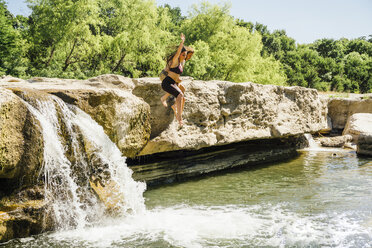 Kaukasisches Paar springt von Felsen in der Nähe von Wasserfällen - BLEF01558