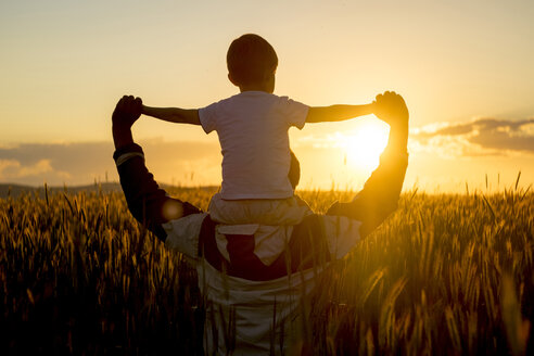 Vater trägt Sohn auf den Schultern in einem Weizenfeld bei Sonnenuntergang - BLEF01618