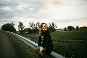 Caucasian woman sitting on guardrail near road - BLEF01630