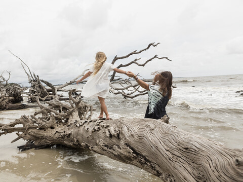 Kaukasische Mutter und Tochter gehen am Strand auf Treibholz, lizenzfreies Stockfoto