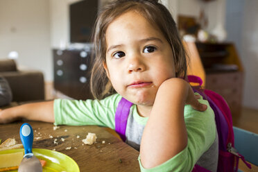 Unordentliches gemischtrassiges Mädchen isst Essen und trägt Rucksack am Tisch - BLEF01668