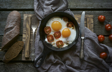 Eggs and tomatoes in frying pan on wooden table - BLEF01687