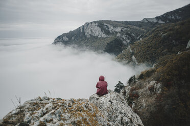 Entfernte kaukasische Frau sitzt auf einem Felsen und beobachtet den Nebel auf dem Meer - BLEF01722