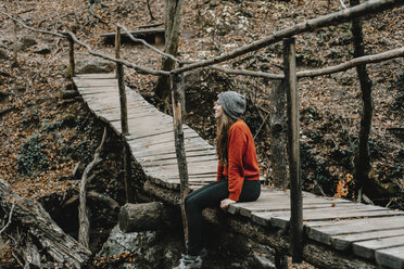 Caucasian woman sitting on footbridge in woods - BLEF01723