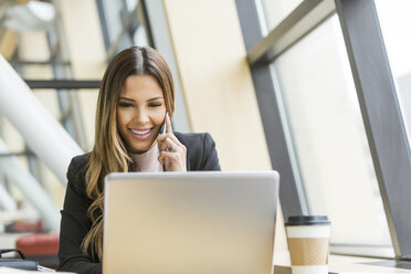 Mixed Race businesswoman talking on cell phone and using laptop - BLEF01732