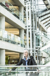 Portrait of pensive Caucasian businesswoman leaning on railing in lobby - BLEF01740