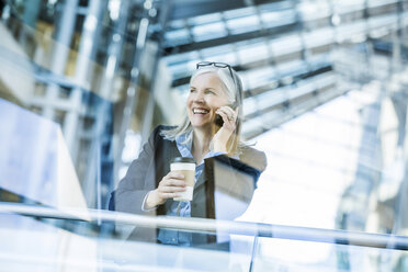 Caucasian businesswoman talking on cell phone leaning on railing in lobby - BLEF01741