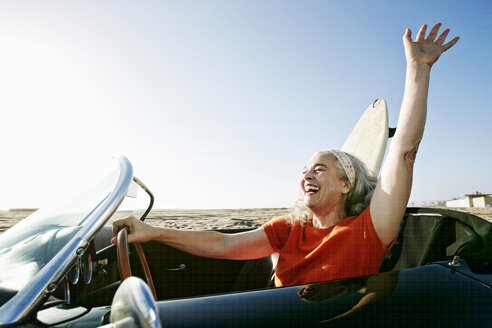 Older Caucasian woman in convertible car with surfboard on beach - BLEF01752