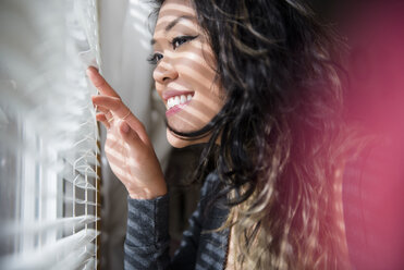 Mixed Race woman peeking out window behind blinds - BLEF01775