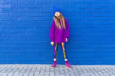 Portrait of girl wearing blue cap and oversized pink pullover standing in front of blue wall - ERRF01195