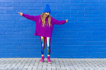 Mädchen mit blauer Mütze und übergroßem rosa Pullover steht vor einer blauen Wand und singt - ERRF01197