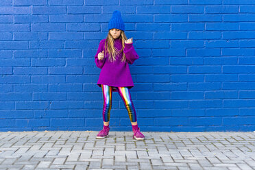 Mädchen mit blauer Mütze und übergroßem rosa Pullover steht vor einer blauen Wand und tanzt - ERRF01198