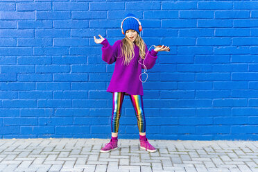 Singing girl wearing oversized pink pullover listening music with headphones in front of blue wall - ERRF01211