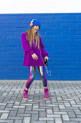 Singing and dancing girl listening music with headphones in front of blue wall - ERRF01214