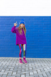 Girl wearing blue cap and oversized pink pullover listening music with headphones in front of blue wall - ERRF01216