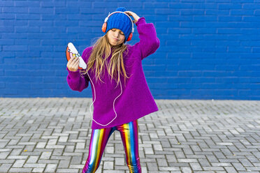 Portrait of girl dancing outdoors while listening music with headphones and smartphone - ERRF01220