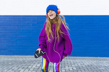 Portrait of happy girl singing while listening music with headphones and smartphone - ERRF01222