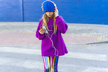 Mädchen mit blauer Mütze und übergroßem rosa Pullover hört Musik mit Kopfhörern und Smartphone - ERRF01225