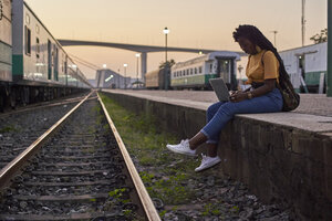 Junge Frau sitzt auf dem Bahnsteig im Bahnhof und benutzt einen Laptop - VEGF00117