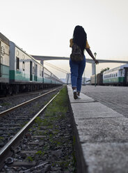 Rückansicht einer jungen Frau, die am Rande der Gleise am Bahnhof spazieren geht - VEGF00135