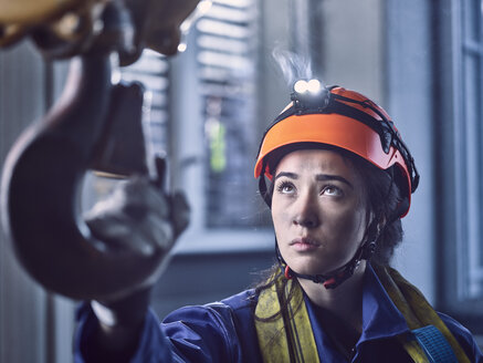 Junge Industriearbeiterin mit Schutzhelm nimmt den Haken eines Hallenkrans - CVF01123