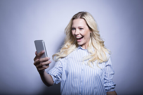 Porträt einer glücklichen blonden Frau, die auf ihr Smartphone schaut, lizenzfreies Stockfoto
